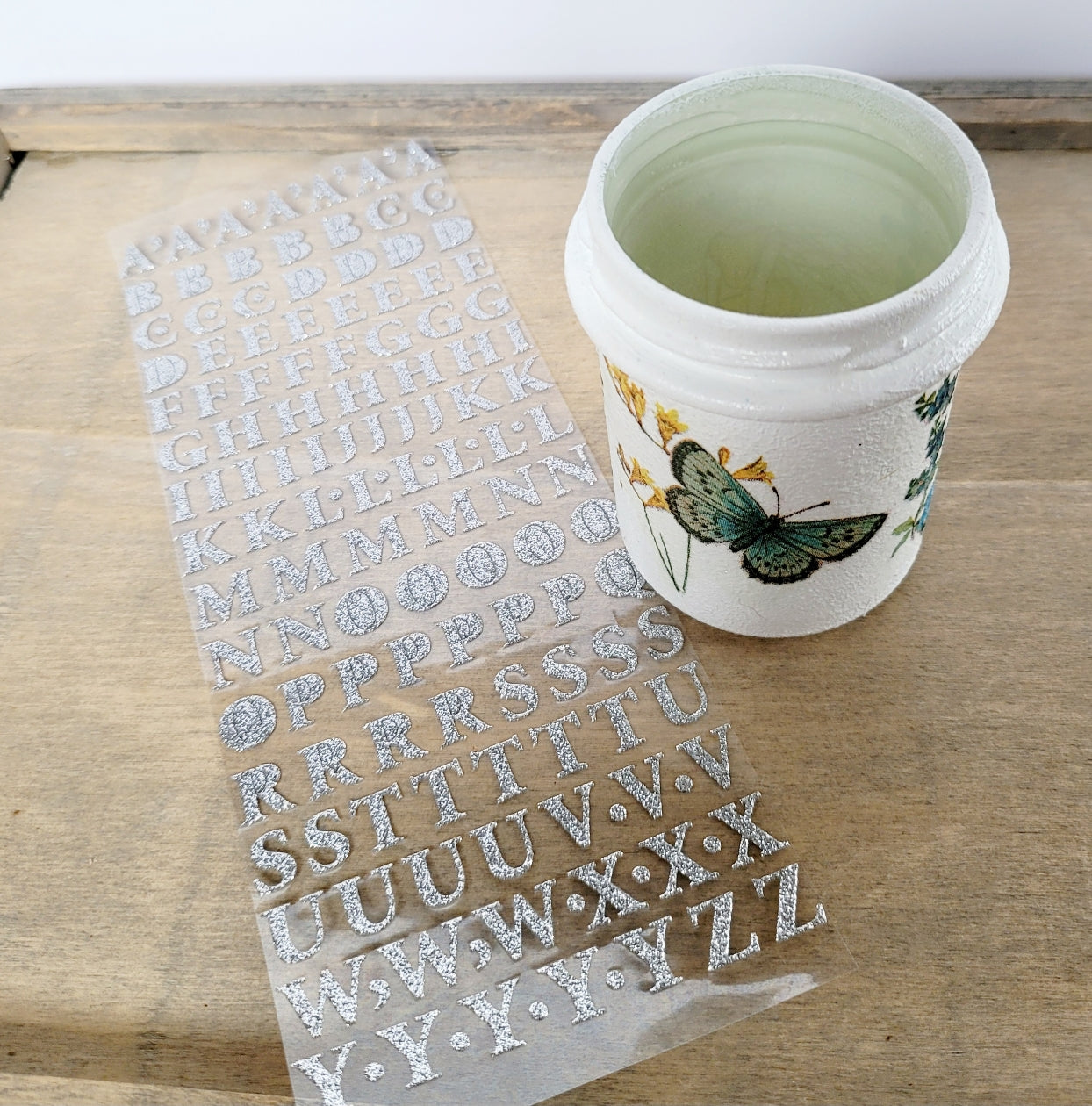 silver sticker sheet with letters and a white painted jar with green butterfly detail