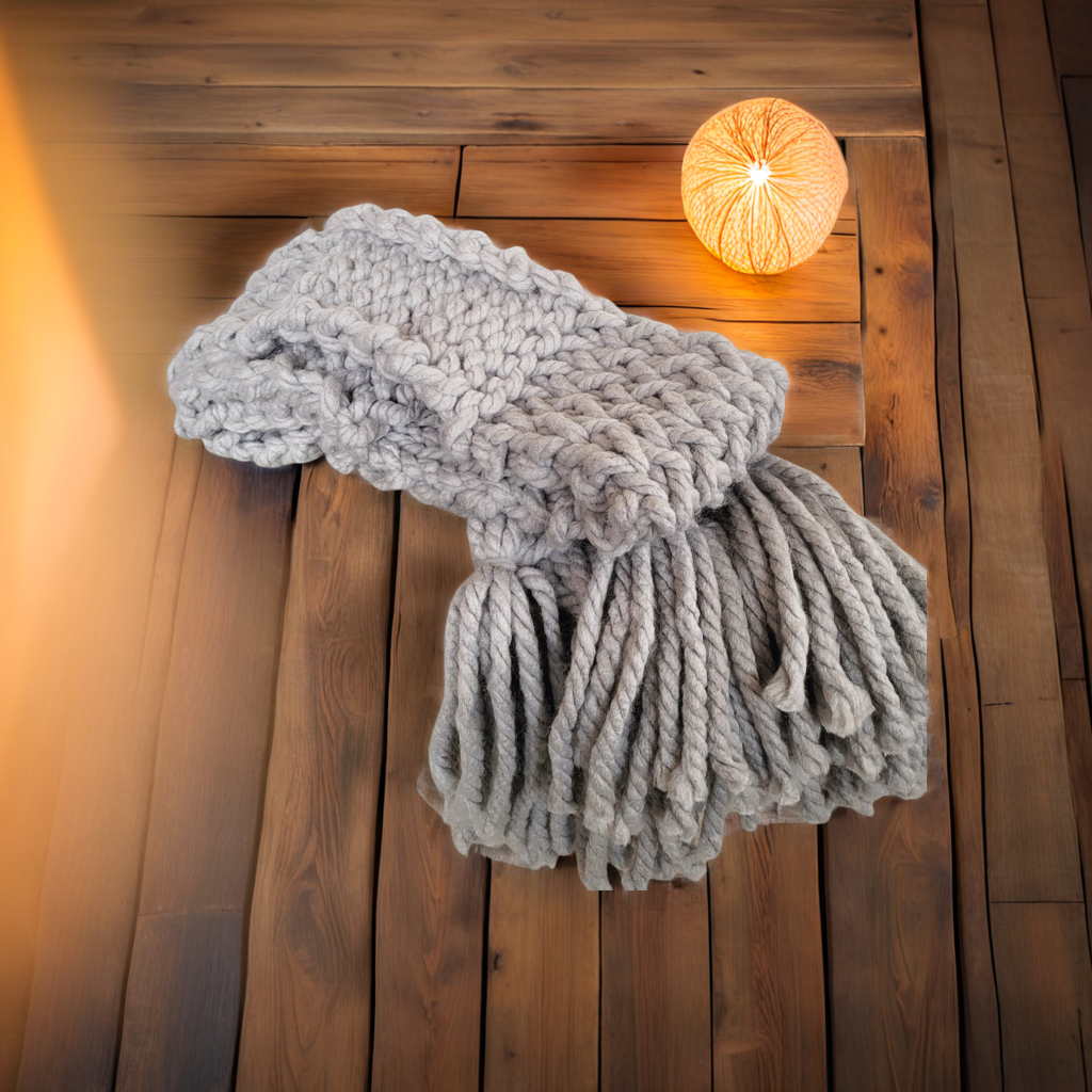 Grey chunky knit scarf with long tassels laid on a wooden tale