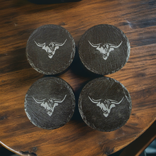 Load image into Gallery viewer, Four black slate coasters with cows head engraving on a wooden surface
