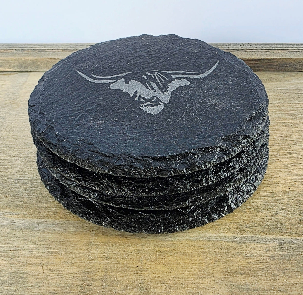 Stack of black slate coasters with a cows head design on a wooden surface