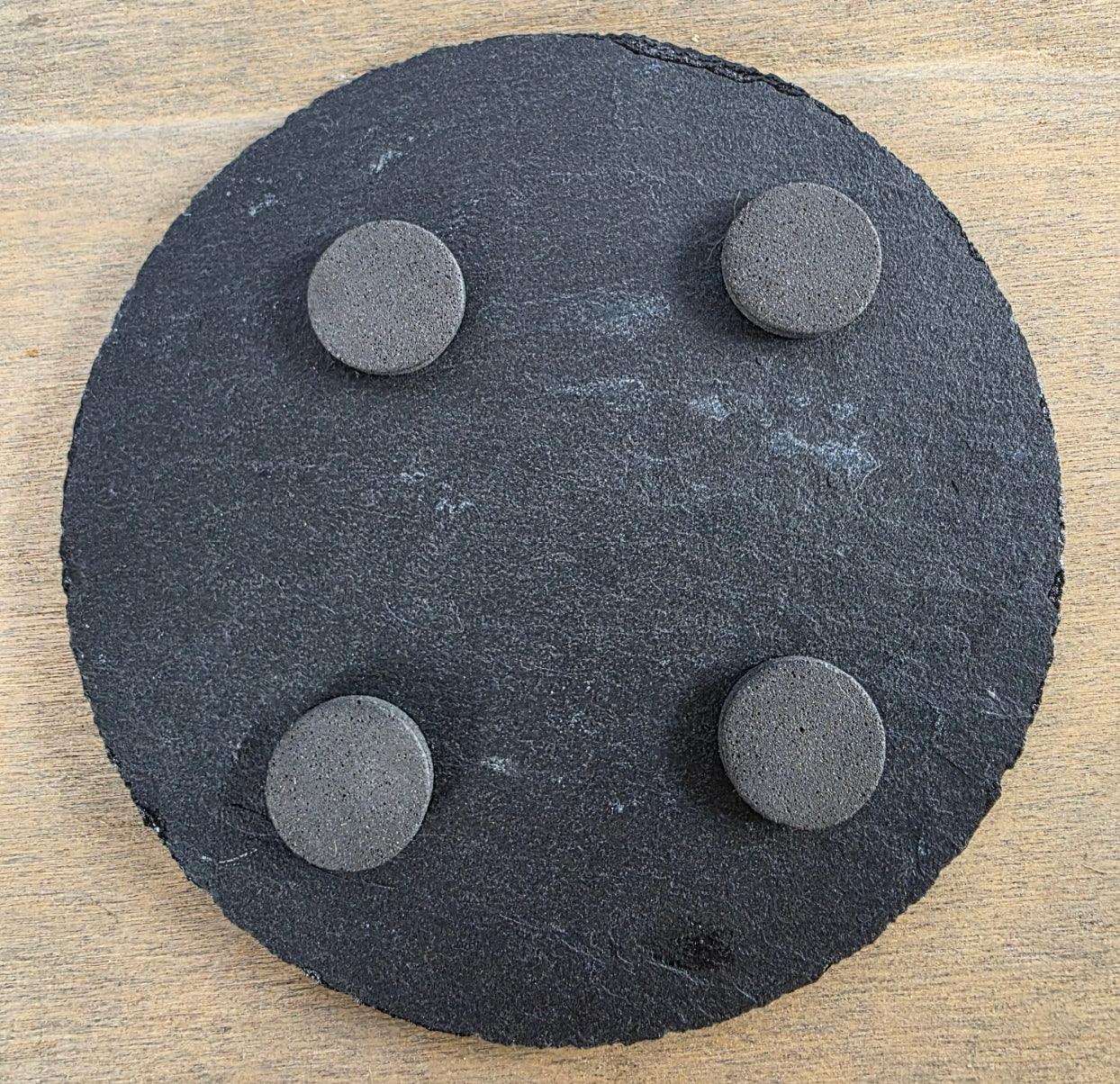 Round black slate coaster with four pads on the underside