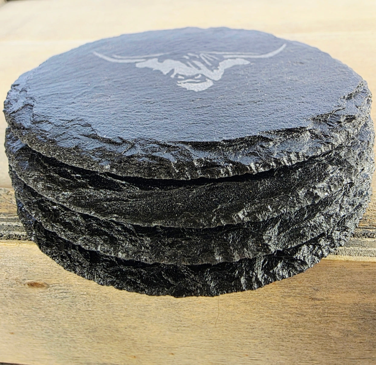 Set of four, round slate coasters with a cows head design on a wooden surface