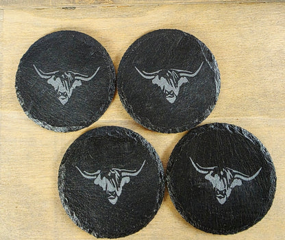 Four black coasters with cow's head design on a wooden surface