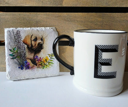 Mug with letter 'E' next to a white slate coaster with golden labrador puppy illustration next to a wooden surface