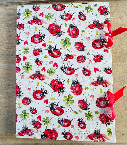 notebook with ladybug pattern on a wooden surface. bound with red ribbon