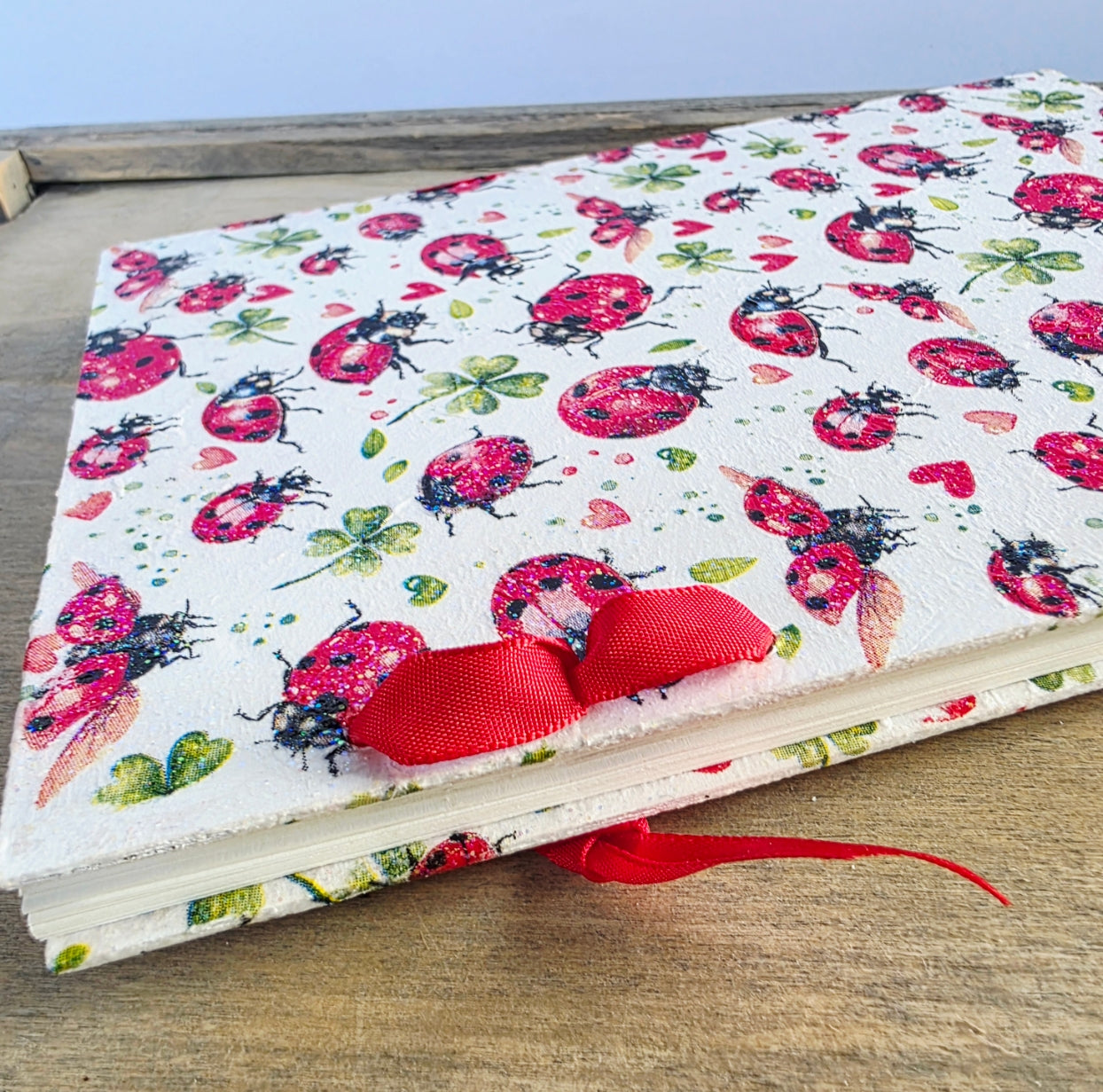Notebook with ladybug pattern and red ribbon on a wooden surface