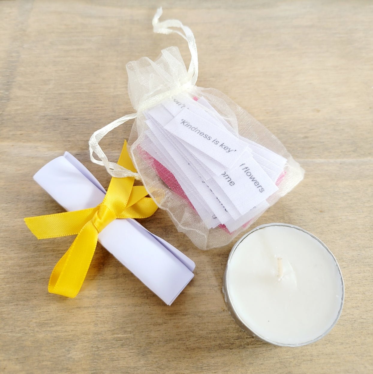 pale organa bag with white paper quotes inside. White rolled up piece of paper tied with yellow ribbon. White tealight candle