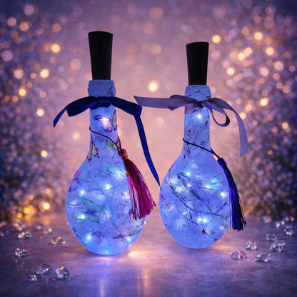 Two decorative miniature bottles with LED lights and bird design on a sparkling background