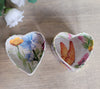 Two heart-shaped boxes with floral and butterfly designs on a wooden surface.