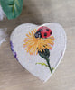 Heart-shaped decorative item with a ladybug and flower design on a wooden surface