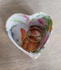 Heart-shaped decorative box with floral patterns containing three rings on a wooden surface