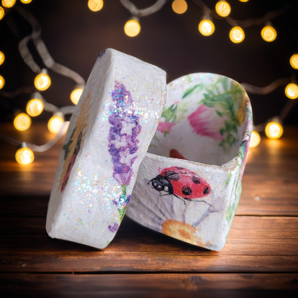 Two decorative boxes with artistic designs on a wooden surface with string lights in the background.