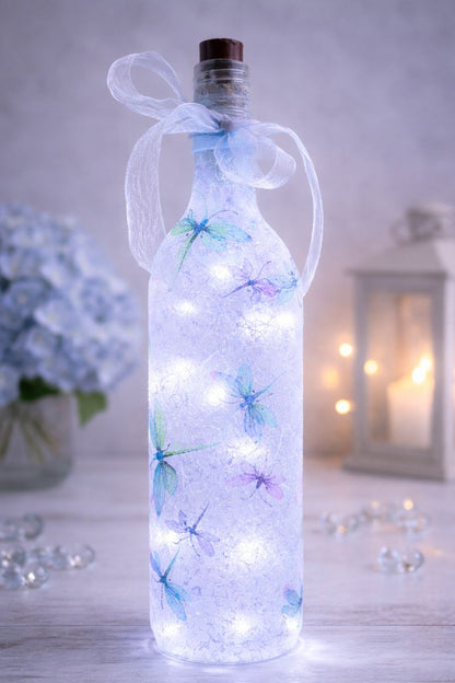 Decorative bottle with LED lights and dragonfly decorations on a wooden surface.