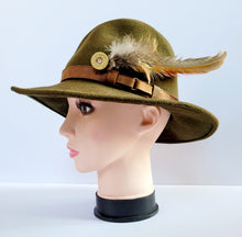 Load image into Gallery viewer, Pheasant feather hat pin, long pheasant tail feather with shorter feathers on the end of a brass gold coloured shotgun cartridge. Shown pinned onto the side of a green trilby style hat
