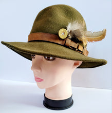 Load image into Gallery viewer, Pheasant feather hat pin, long pheasant tail feather with shorter feathers on the end of a brass gold coloured shotgun cartridge. Shown pinned on the side of a green trilby style hat
