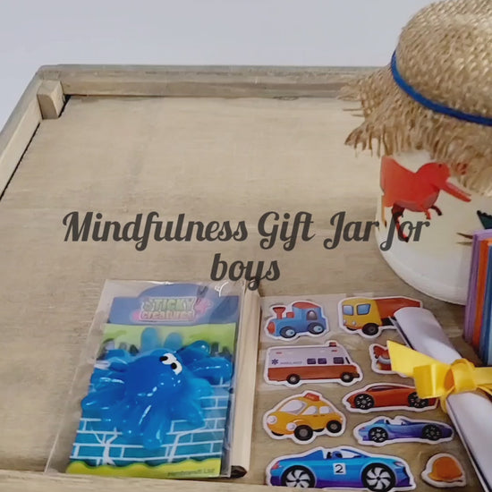 Video of a White painted jar with Dinosuar detail. Hessian lid secured with a blue band, sticker sheet, blue sticky toy, lit up flameless votive candle, white rolled up note secured with yellow ribbon, key ring attached to jar with a green Dinosaur on it. Coloured card scrapbook and short brown pencil, organza bag containing pink and blue quotes