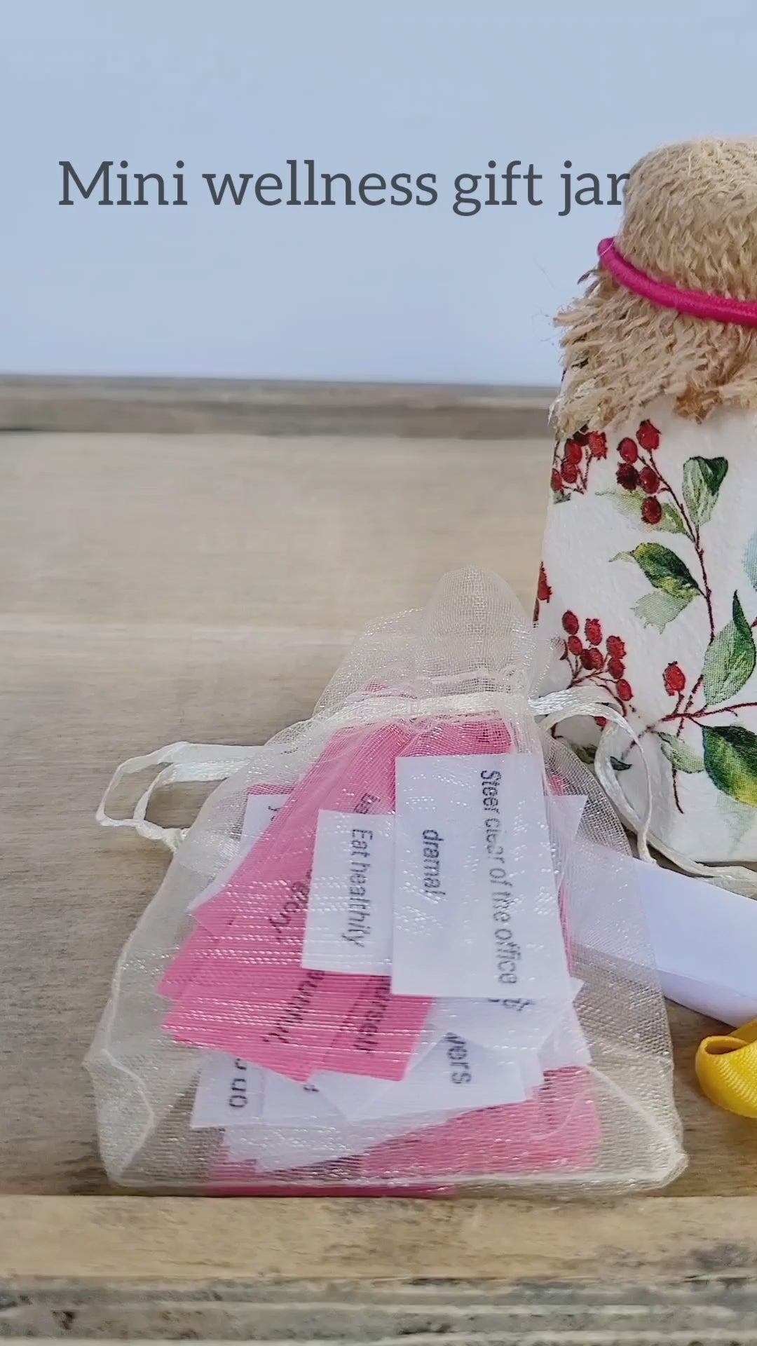 video showing a small white jar decorated with red berries and leaves, an organza bag with white and paper quotes inside. Jar has hessian lid in light brown, small white tealight candle and a white rolled up pice of paper tied with yellow ribbon