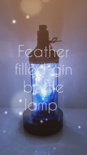 Load and play video in Gallery viewer, Rotating example of a Lit up blue glass gin bottle with jute twine detail around the top of the lamp, cork LED lights. Bottle is filled with blue and white feathers and blue coloured stones in the bottom.
