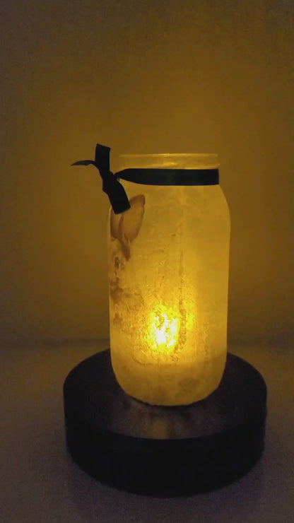 Rotating example of a Lit up glass jar with Hares in the snow detail, flameless candle and green bow