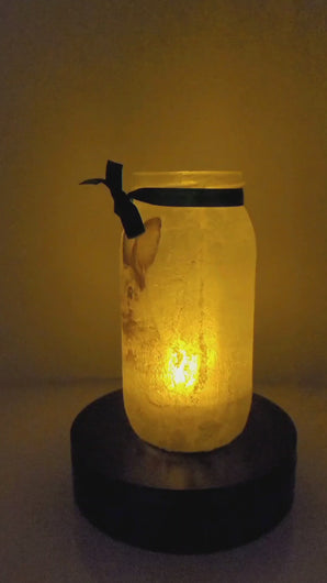 Rotating example of a Lit up glass jar with Hares in the snow detail, flameless candle and green bow