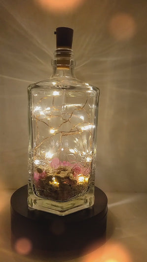 Rotating example of a Lit up hexagonal bottle with pink and gold coloured stones inside. Cork LED lights