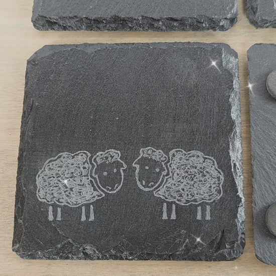 video of four slate square coasters with two sheep on each. sheep are facing eachother