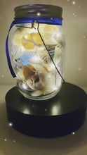Load and play video in Gallery viewer, Jar filled with shells, pebbles and coloured glass stones. Lit up with lid and carry handle. Blue decorative ribbon
