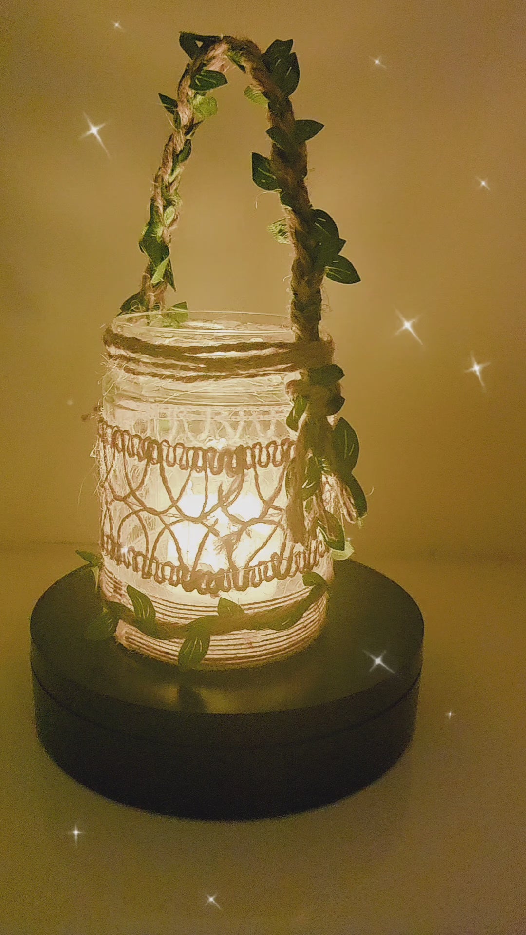 Video of a rotating Decorative lantern with decorative burlap design. Jute handle with leaves glowing light on a table in a cozy living room setting.