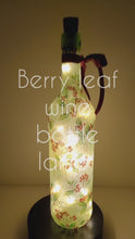 Load and play video in Gallery viewer, A rotating example of a Lit up wine bottle with green leaf and red berry detail. Cork LED lights and red ribbon embellishment.
