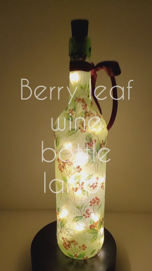 A rotating example of a Lit up wine bottle with green leaf and red berry detail. Cork LED lights and red ribbon embellishment.