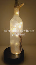 Load and play video in Gallery viewer, Rotating wine bottle, lit up with brown Highland cow detail. Gold bow finish.

