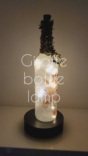 Rotating example of a Lit up wine bottle with single Giraffe detail and cork LED lights. Giraffe is holding a flower in its mouth. Jute twine with leaves is wrapped around the neck of the bottle