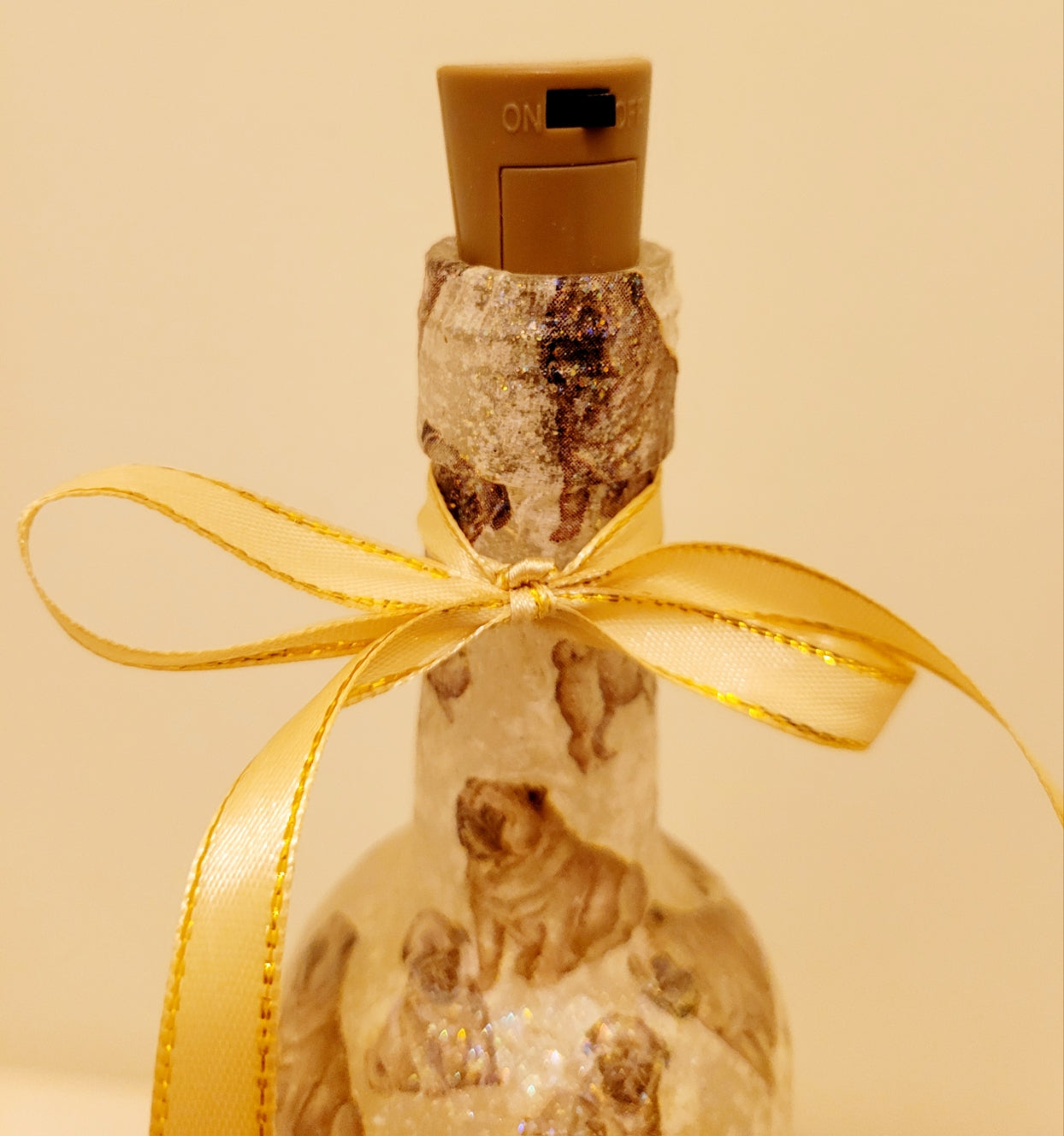 Gold ribbon embellishment around the neck of a wine bottle. Brown cork with black on/off switch