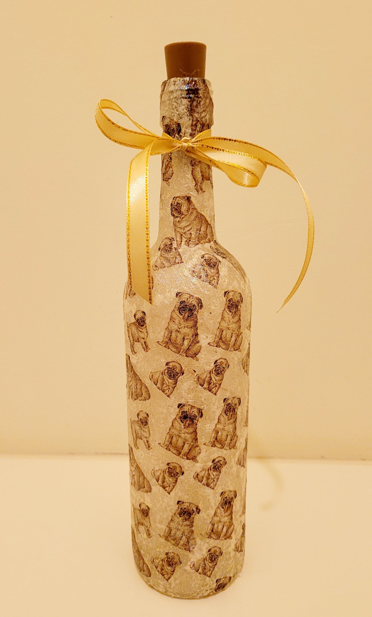 wine bottle decorated with tiny pug dog images. Cork LED lights and gold ribbon embellishment. Shown unlit