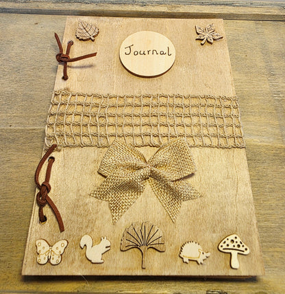 handmade rustic journal with wooden outercovers embellished with woodland creatures and wooden leaves. Burlap mesh decoration across the front, bound with brown suede, decorative hessian bow