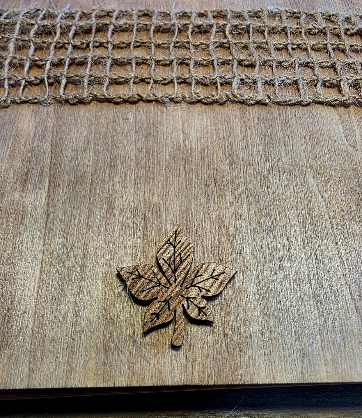 Wooden leaf-shaped object on a wooden journal surface with woven texture at the top.