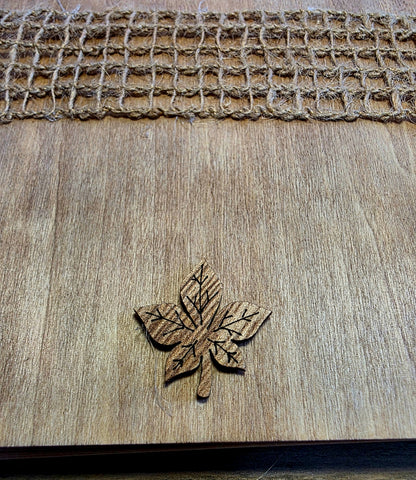 Wooden leaf-shaped object on a wooden journal surface with woven texture at the top.