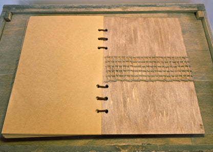 Open notebook with wooden cover on a wooden surface. Burlap mesh decoration on the inside back cover. Brown plain pages