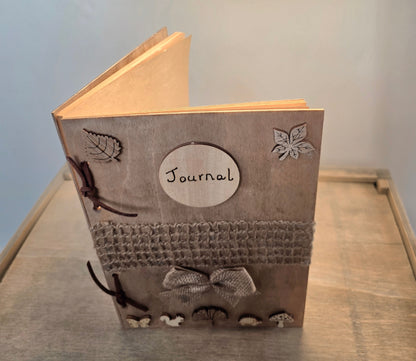 handmade rustic journal with wooden outercovers embellished with woodland creatures and wooden leaves. Burlap mesh decoration across the front, bound with brown suede, decorative hessian bow. Standing on its end and slightly open