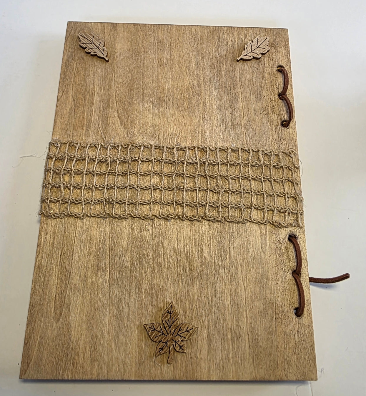 Wooden journal back cover with leaf designs and burlap mesh decoration across the middle, on a white background