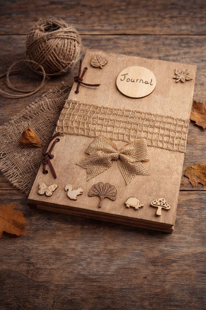handmade rustic journal with wooden outercovers embellished with woodland creatures and wooden leaves. Burlap mesh decoration across the front, bound with brown suede, decorative hessian bow