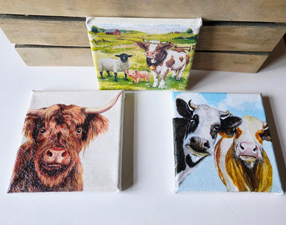 set of three decoupage pictures on stretched white canvas. 1. A highland cow. 2. A black and  white cow and a brown and white cow looking nosey. 3. A sheep, pig and cow standing in a meadow