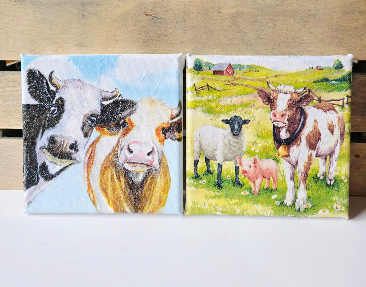set of two farmyard animal decoupage pictures on stretched white canvas. One is a cow, sheep and pig in a meadow
 the other two cows; one black and white, one brown and white looking nosey