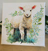 Canvas print of a lamb surrounded by flowers and leaves on a wooden surface.
