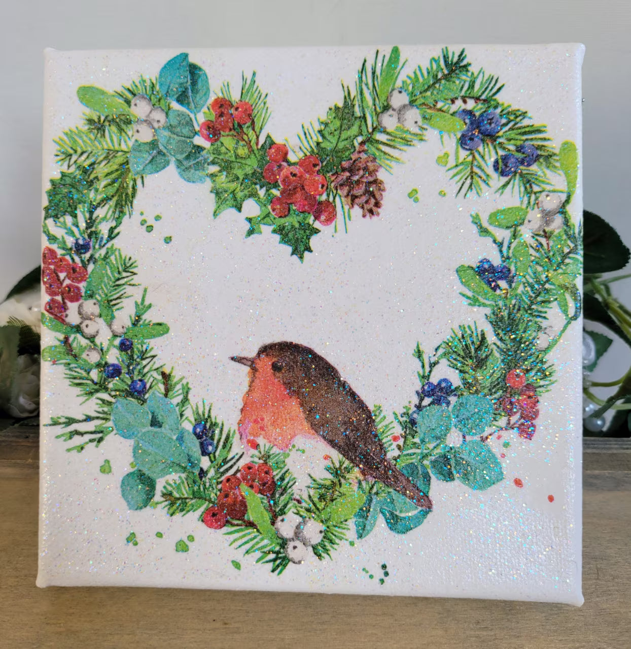 Decoupage artwork on a square canvs with a robin and festive wreath design on a white background.