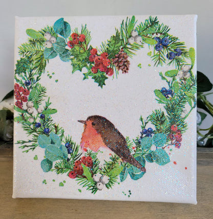 Decoupage artwork on a square canvs with a robin and festive wreath design on a white background.