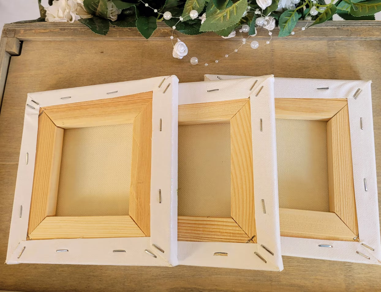 Three square canvases shown from the back/underside showing the wood frames and staples in the canvas, on a wooden surface.