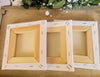 Three square canvases shown from the back/underside showing the wood frames and staples in the canvas, on a wooden surface.