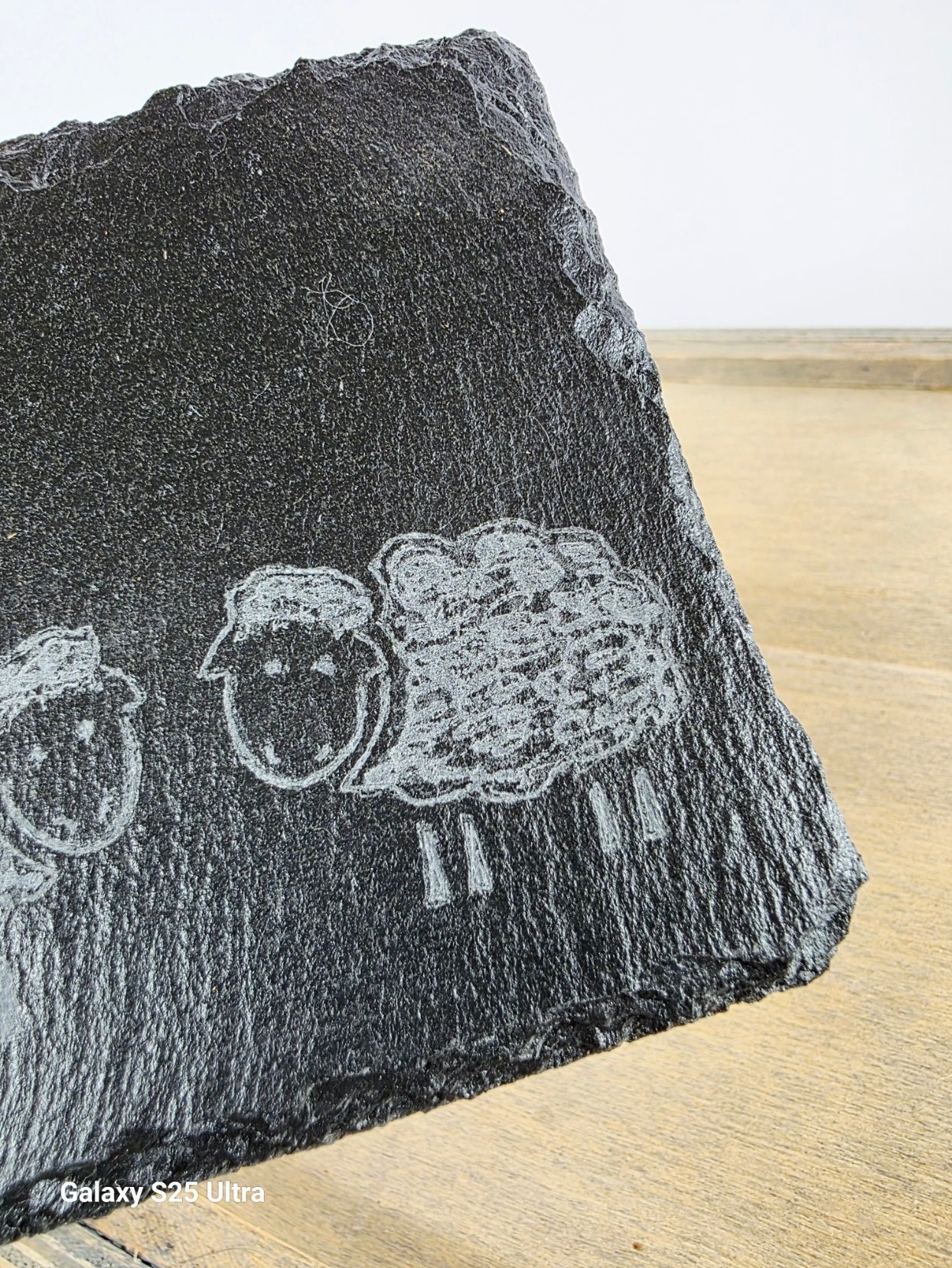 Black stone with engraved sheep design on a wooden surface