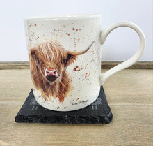 Load image into Gallery viewer, Mug with a highland cow design on a black slate coaster on a wooden surface
